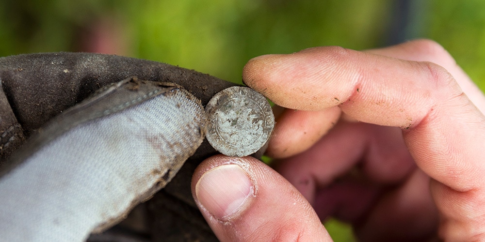 Eine bei der Prospektion gefundene Münze wird zwischen Handschuh und Finger sorgfältig gehalten